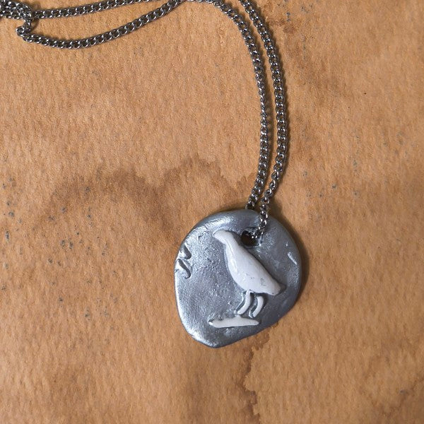 Silver necklace with a pendant featuring a bird design on a brown surface