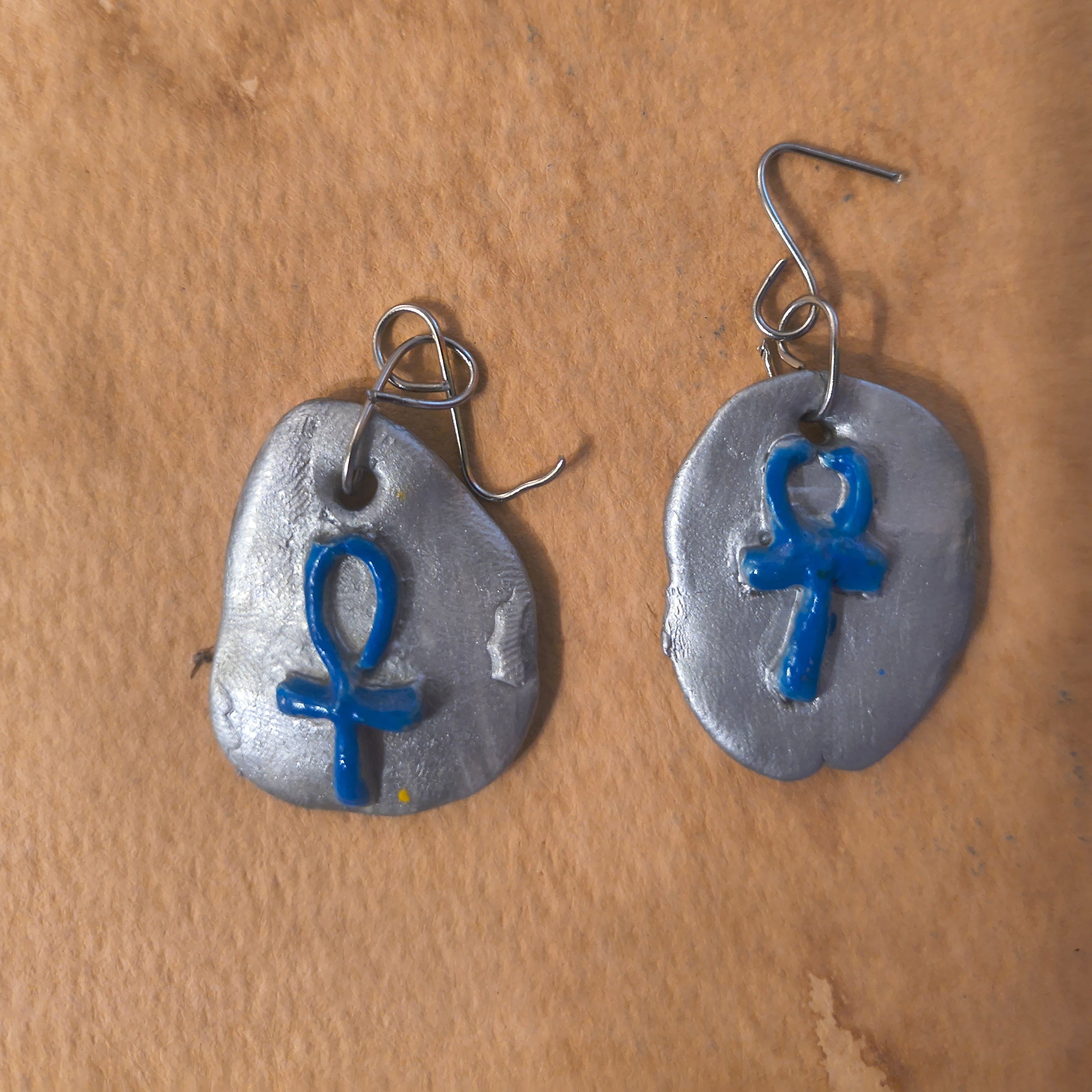 Silver earrings with blue ankh ymbols on a brown surface