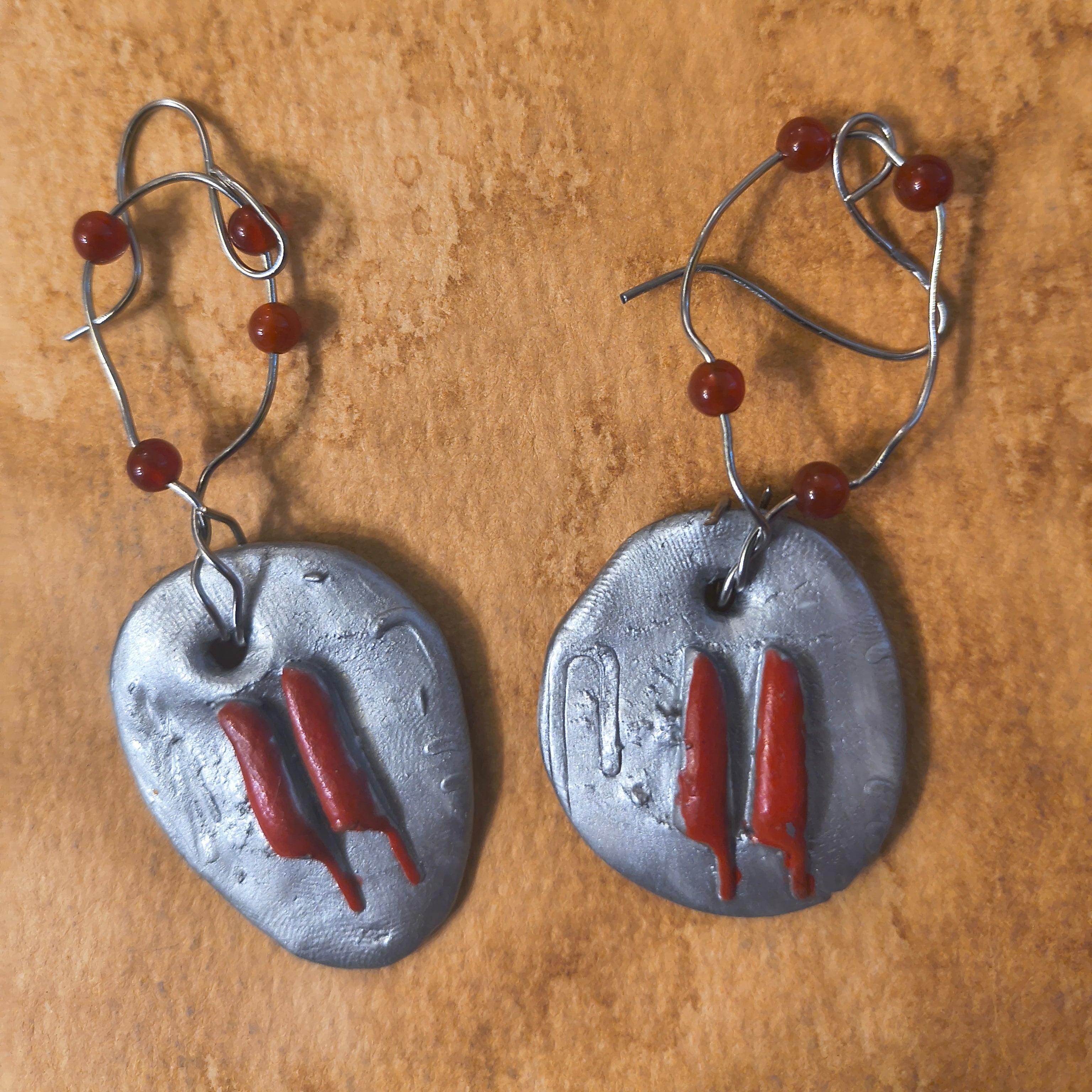 Earrings with red knife hieroglyphics. Each earring has four red beads. Sitting on a brown surface. 