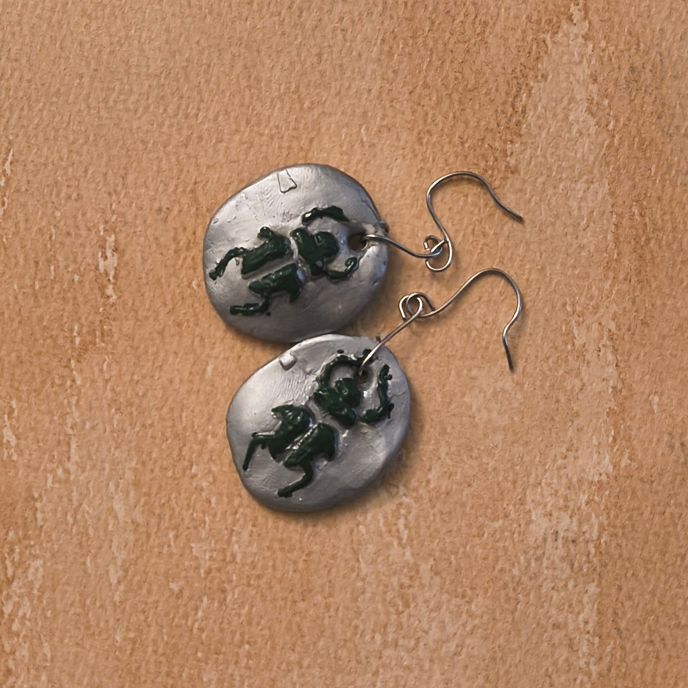 Silver earrings with green beetle designs on a brown background