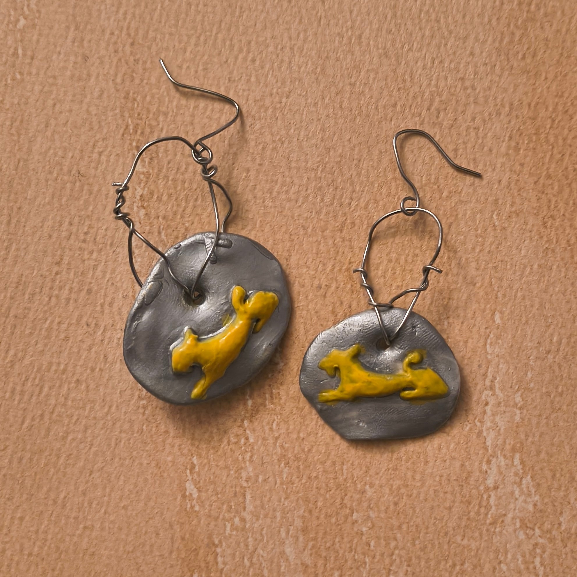 Pair of wire earrings with yellow lion figures on silver circular pendants against a brown background