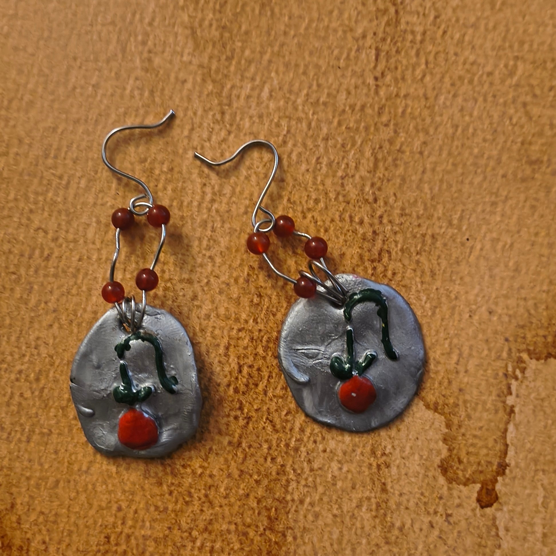 Pair of silver earrings with cherries and four red beads on a brown surface